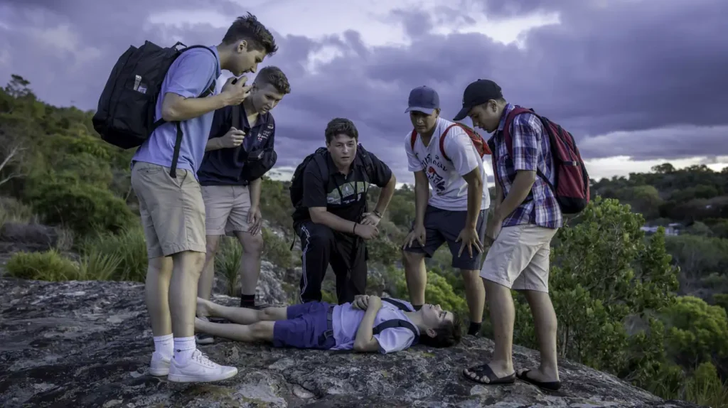 a group of teenage boys crowd around an injured friend